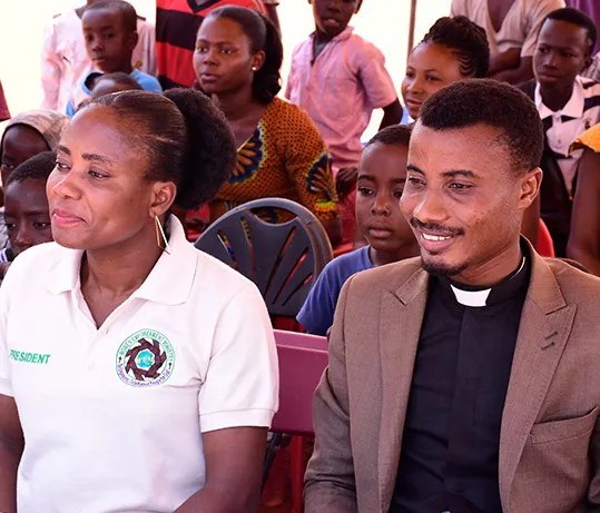 A ministry member in a GWEM polo shirt and a minister in a clerical collar seated in the front row of an audience.