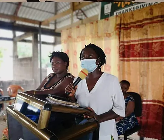 A woman in a face mask speaking into a microphone at a lectern during an indoor health education session.