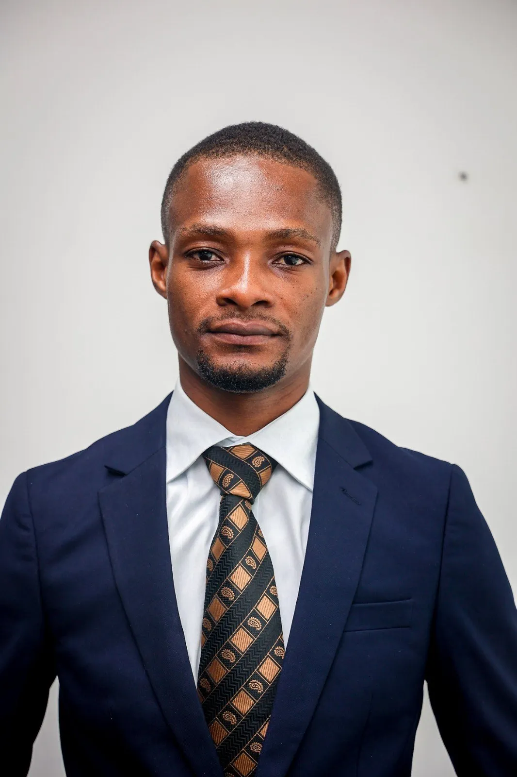 Solomon Kyei Mensah wearing a dark suit, white shirt and a black and gold patterned tie.